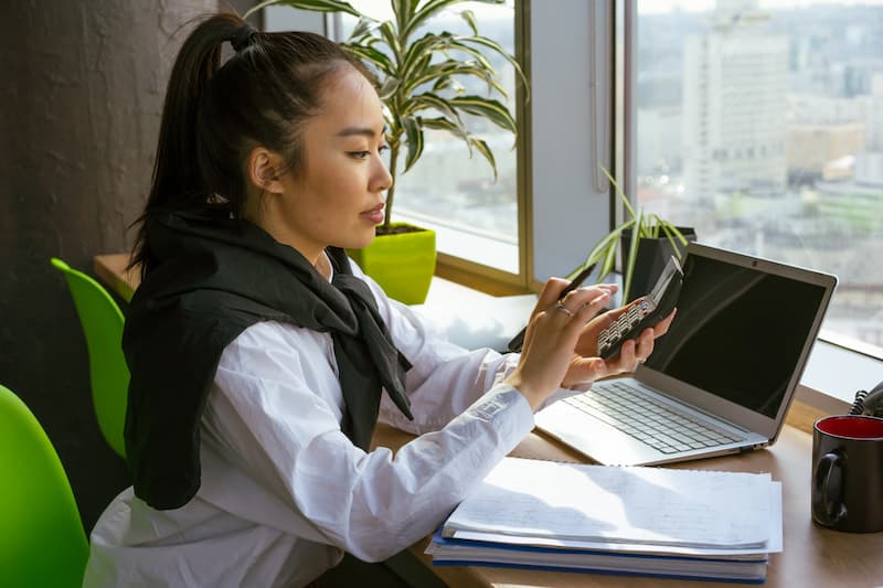 seorang perempuan menggunakan kalkulator di depan laptop